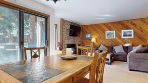 A cozy living room with a stone fireplace, wooden walls, a dining table, and a sofa.