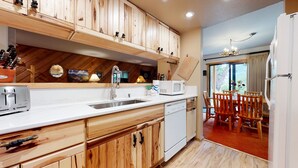 A kitchen with wooden cabinets, a sink, a microwave, and a dishwasher. There is a dining area with a table and chairs. - Pet-Friendly Quiet Corner Cabin, Relaxing Location. Near Beautiful Trails (Mammoth Lakes)