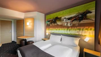 A modern hotel room with a large bed, a desk, and a wall-mounted TV displaying a horse race.