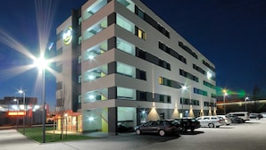 Een hotel met meerdere verdiepingen, met een modern ontwerp, voorzien van balkons en een parkeerplaats met verschillende auto's.