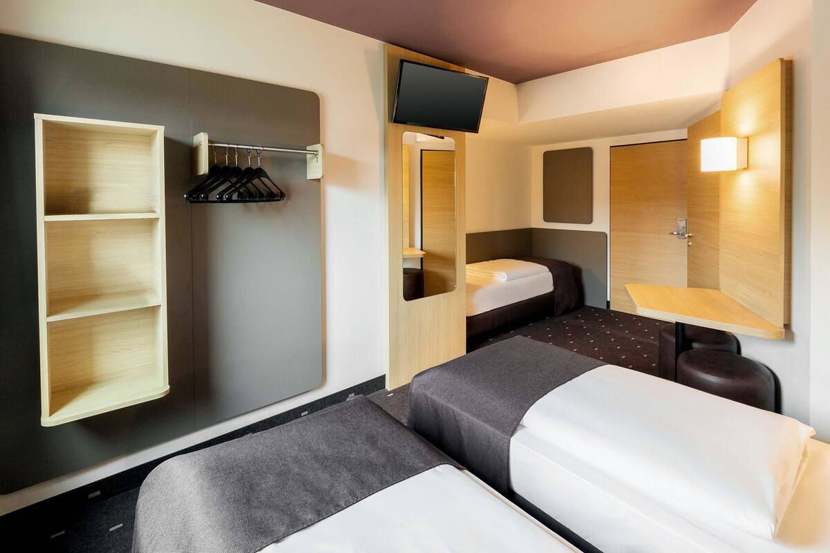 Ein kleines Hotelzimmer mit zwei Betten, einem Kleiderschrank, einem Fernseher und einem Spiegel.
