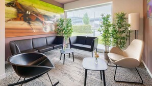Un espace d’attente moderne, doté de canapés en cuir, d’un fauteuil noir, d’une petite table avec un vase et d’une grande fenêtre donnant sur l’extérieur.