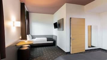 Ein modernes Hotelzimmer mit einem Bett, einer Couch, einem Schreibtisch mit Lampe, einem Fernseher und einer Tür.