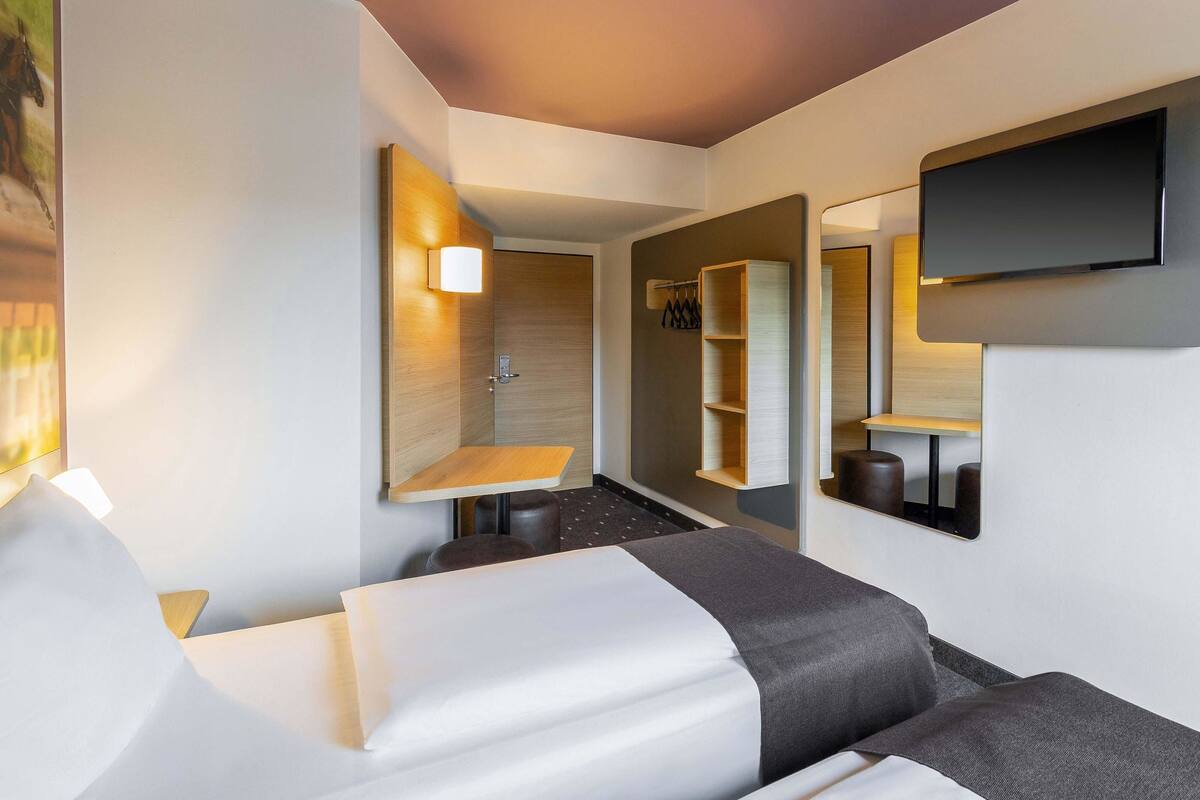 Ein modernes Hotelzimmer mit Bett, Sitzecke, Spiegel und Fernseher.