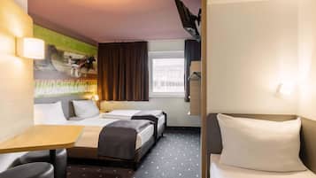 Ein Hotelzimmer mit zwei Betten, einem Schreibtisch und einem Stuhl. Ein Fenster mit Vorhängen, eine Wandleuchte und ein Bild an der Wand sind ebenfalls vorhanden.