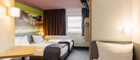 A hotel room with two beds, a desk, and a chair. There is a window with curtains, a wall-mounted lamp, and a painting on the wall.