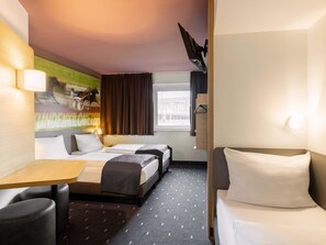 Une chambre d’hôtel avec deux lits, un bureau et une chaise. Il y a une fenêtre avec des rideaux, une lampe fixée au mur et un tableau accroché au mur.