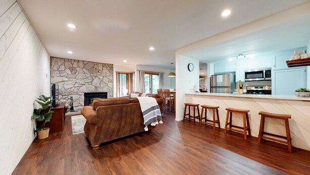 A modern living room with a stone fireplace, a sofa, and a dining area with wooden stools. - Pet-Friendly. Updated, Private Gas Grill, Located in the Quiet Meadow Area (Mammoth Lakes)