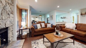 A modern living room with a stone wall, two brown leather sofas, a wooden coffee table, and a fireplace. - Pet-Friendly. Updated, Private Gas Grill, Located in the Quiet Meadow Area (Mammoth Lakes)