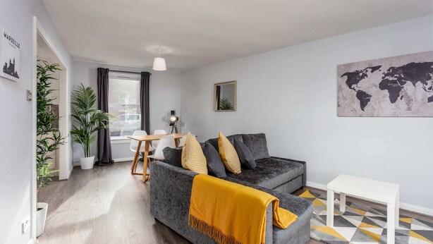 Una sala de estar moderna con un sofá gris, un cojín amarillo, una mesa de centro blanca y un mapa del mundo en la pared.