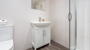 Un baño moderno con lavamanos blanco, espejo y cabina de ducha de vidrio.
