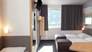 Habitación de hotel con cama, escritorio, silla, televisor montado en la pared y ventana con cortinas.