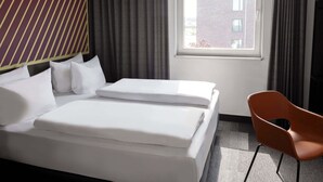 Habitación de hotel con una cama, una silla, un ventanal y vista a un edificio.