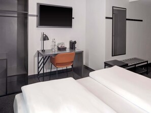 Habitación de hotel con una cama, un escritorio con silla, un televisor, una cafetera y una mesita.