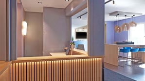 Una zona de recepción moderna con un mostrador de madera, un área de descanso con sillas azules y un amplio ventanal que proporciona luz natural.