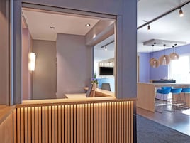 Una zona de recepción moderna con un mostrador de madera, un área de descanso con sillas azules y un amplio ventanal que proporciona luz natural.