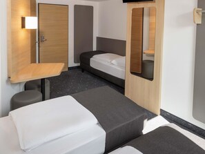 Una habitación de hotel pequeña con cama, un escritorio, una silla, una mesita de noche y un espejo.