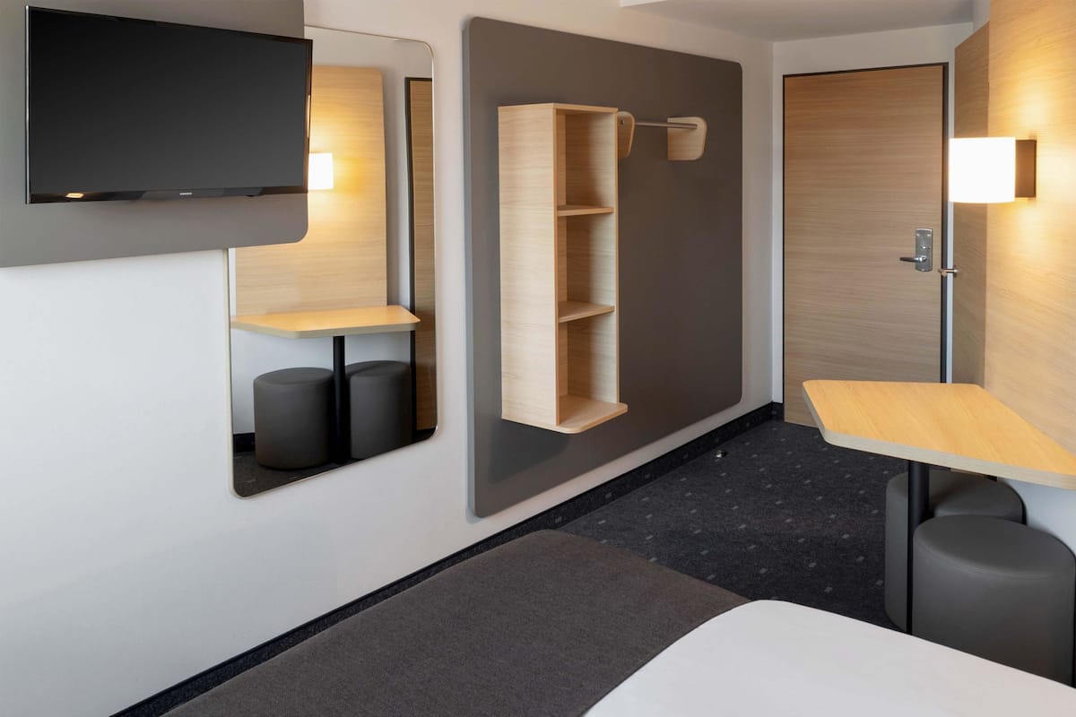 Una habitación de hotel moderna con una cama, un escritorio, un espejo y estanterías empotradas.