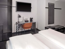 Habitación de hotel con una cama, un escritorio con silla, un televisor, una cafetera y una mesita.