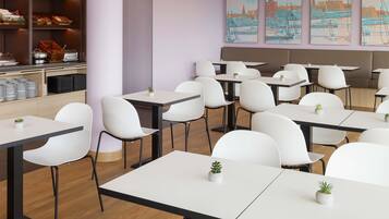Un espace de restauration moderne avec des chaises et des tables blanches, un comptoir où sont exposées des pâtisseries et des tableaux représentant des paysages urbains accrochés au mur.