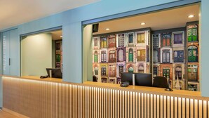 A reception area with a modern design, featuring a wooden reception desk and a wall with colorful architectural illustrations. - B&B HOTEL Lübeck-Hbf (Lübeck)