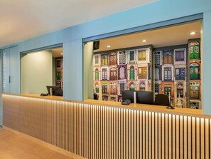 A reception area with a modern design, featuring a wooden reception desk and a wall with colorful architectural illustrations. - B&B HOTEL Lübeck-Hbf (Lübeck)