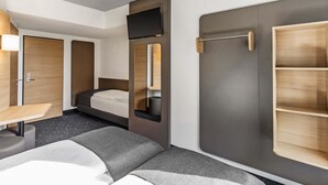 A compact hotel room with a bed, a desk, and a wardrobe. - B&B HOTEL Lübeck-Hbf (Lübeck)