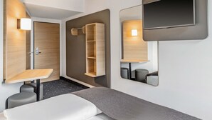 A modern hotel room with a bed, a TV mounted on the wall, a wooden wardrobe, and a small seating area with stools. - B&B HOTEL Lübeck-Hbf (Lübeck)