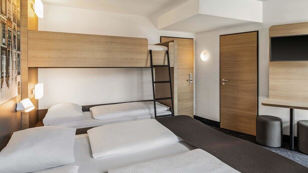 A hotel room with bunk beds, a desk, and a wardrobe. - B&B HOTEL Lübeck-Hbf (Lübeck)