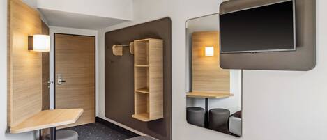 A modern hotel room with a bed, a desk, a mirror, and a TV.
