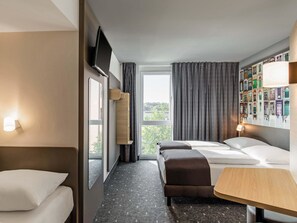 Habitación de hotel con dos camas, una mesita, televisor montado en la pared y una ventana con cortinas.