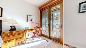 Une pièce comprenant un bureau en bois, une chaise, une lampe et une porte-fenêtre coulissante donnant sur un espace extérieur avec une chaise et une table.
