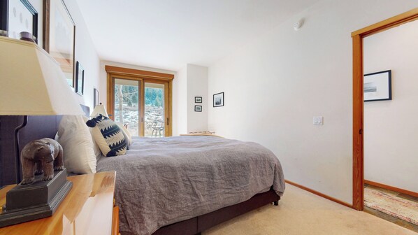 Une chambre à coucher avec un lit, une table de chevet, une lampe et une fenêtre donnant sur des arbres.