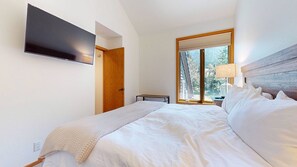 A bedroom with a bed, a television mounted on the wall, a window with a view of trees, and a door.