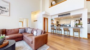 A modern living room with a brown sectional sofa, a kitchen with a bar area, and a large window. - Pet-Friendly, Nicely Furnished, 2 Primary Suites & Private Washer/Dryer (Mammoth Lakes)