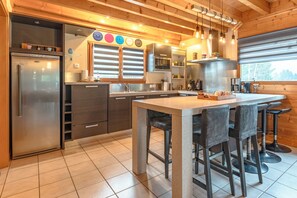Eine moderne Küche mit einer zentralen Kochinsel, Barhocker und einem Edelstahl-Kühlschrank.