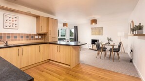A modern kitchen with wooden cabinets, a black countertop, and a dining area with a table and chairs. - Walker Suite No53 - Donnini Apartments (Kilmarnock)