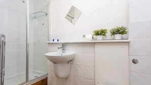 A bathroom with a glass shower enclosure, a sink with a mirror above it, and a toilet. There are three potted plants on a shelf above the sink. - Walker Suite No53 - Donnini Apartments (Kilmarnock)