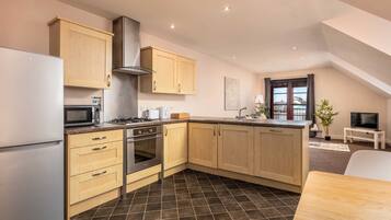 A modern kitchen with light wooden cabinets, stainless steel appliances, and a tiled floor.