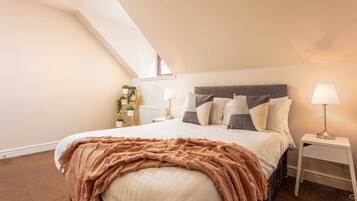 A bedroom with a large bed, a skylight, a bedside table with a lamp, and a small plant.
