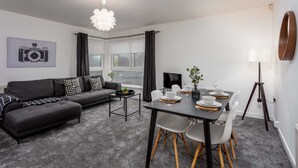 A modern living room with a sofa, dining table, and chairs. There is a camera on the wall, a lamp, and a plant on the table. - Walker Suite No73 - Donnini Apartments (Kilmarnock)