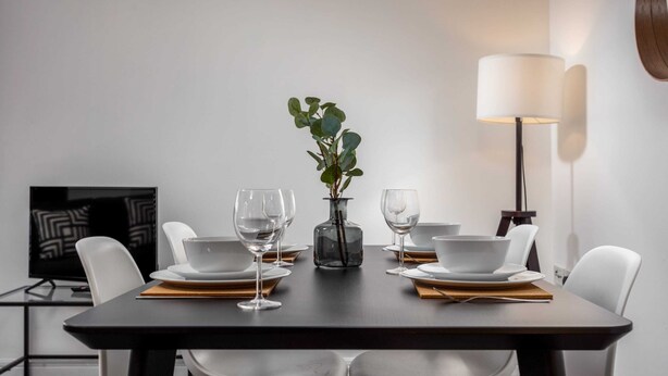 A modern dining area with a dark wooden table, white chairs, and a vase with a plant. - Walker Suite No73 - Donnini Apartments (Kilmarnock)