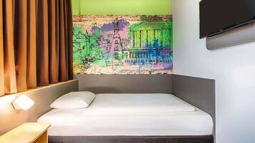 Una habitación de hotel moderna con una cama, una mesita de noche de madera, un televisor montado en la pared y un cuadro abstracto colorido sobre la cama.