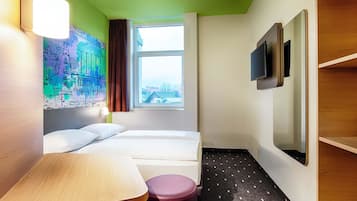 Ein Hotelzimmer mit Bett, Schreibtisch, Stuhl, Fernseher und einem Fenster mit Blick auf Gebäude.