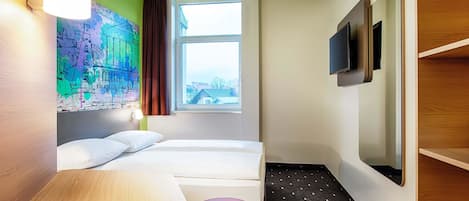 Habitación de hotel con cama, escritorio, silla, televisor y ventana con vista a edificios.