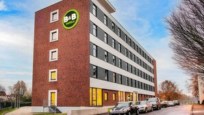 Un hôtel-restaurant de type « bed and breakfast » avec une façade moderne en briques, plusieurs étages et une rangée de voitures garées devant.