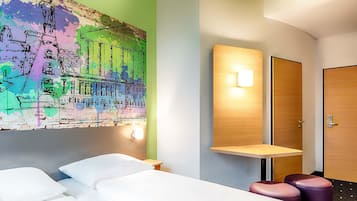 A hotel room with two beds, a colorful mural, a bedside table, a nightstand, a wall-mounted light, and a door.