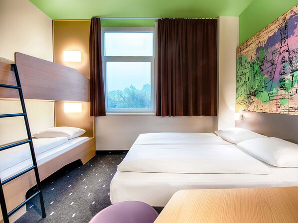 Une chambre d’hôtel avec un lit superposé, un lit simple, une fenêtre avec des rideaux, une carte accrochée au mur et un petit tabouret.
