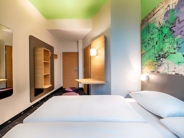 Habitación de hotel con cama, espejo, estante y luz fijada a la pared.