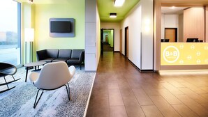 Un espace d’accueil d’hôtel comprenant un comptoir de réception, un coin salon et un téléviseur fixé au mur.